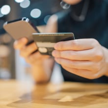 A person holds a phone in one hand and a credit card in another.