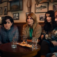 A group of women sit around a pub table looking at a man.