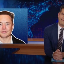 A man in a suit sits behind a talk show desk. In the top-left is an image of another man.