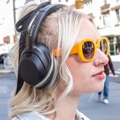 young woman in yellow sunglasses wearing Sony headphones on city street