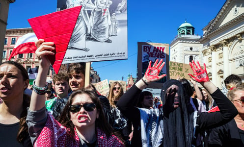 A group of pro-Palestinian protesters gather holding flags, signs, and large red triangles. 