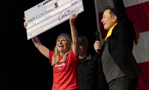 Elon Musk stands on stage cheering for a woman holding up a giant check written out for $1 million.