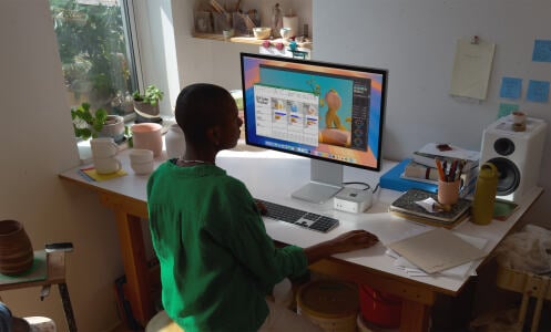 Person sitting at computer desk using Mac Mini and iMac