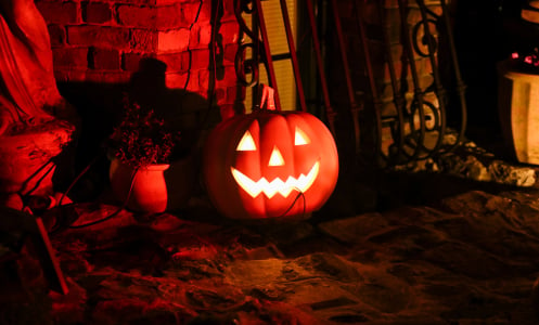 A glowing carved pumpkin sits against a brick wall in the dim light.