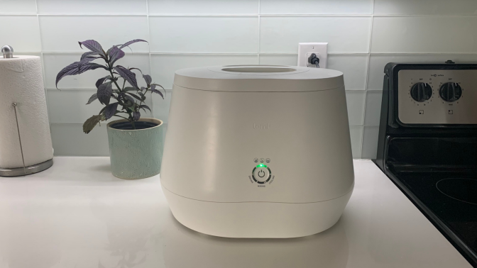 Lomi composter on kitchen counter with plant in the background