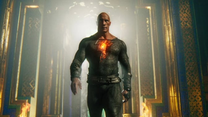 A muscular man wearing a glowing superhero outfit walks forward.