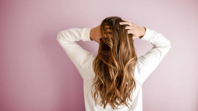 woman with her hands in her light brown hair in front of a pink background