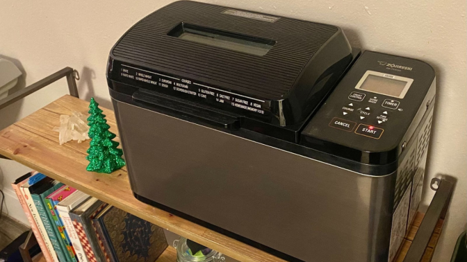 silver and black breadmaker sitting on wooden shelf