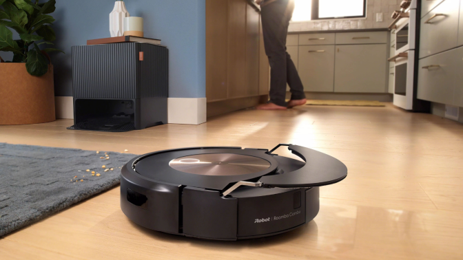 Roomba cleaning hardwood floor and lifting mopping pad with person and iRobot dock in background