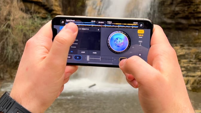 Person holding up a phone with the DJ it! app running, while standing next to a waterfall