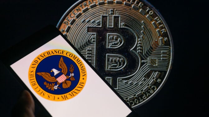 The seal of the U.S. Securities and Exchange Commission is being displayed on a smartphone, with Bitcoin visible on the screen in the background.