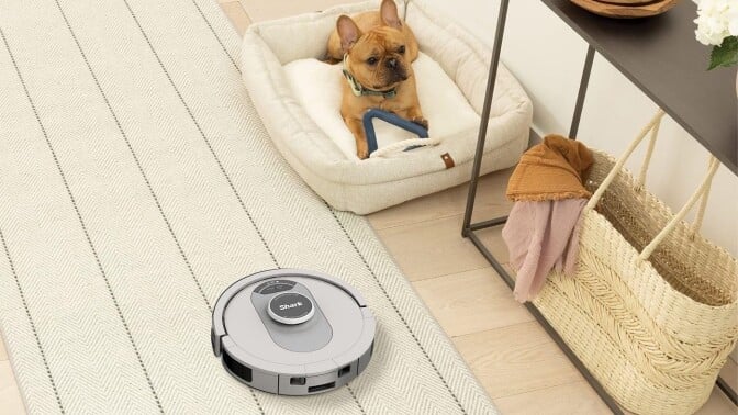 a shark AI ultra robot vacuum goes by a small dog in a bed