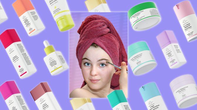 A young white girl with a terry towel wrapped around her hair list a makeup brush to her eye. Around her are a rainbow array of Drunk Elephant products.