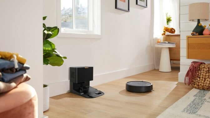 a roomba combo i5+ cleans the floor near its self-emptying dock in a home.