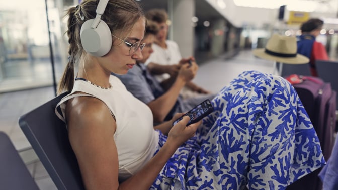 girl on phone in airport terminal wearing sony wh-1000xm5 headphones