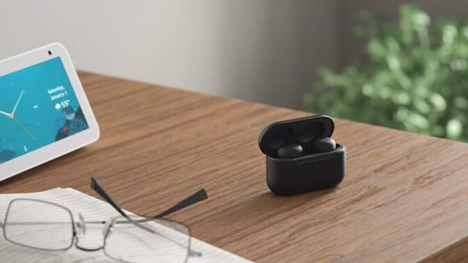 a pair of echo buds sits in their charging case on a desk that also has an open notebook, a pair of glasses, and an echo device