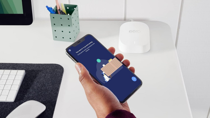 person holding smartphone next to eero router 