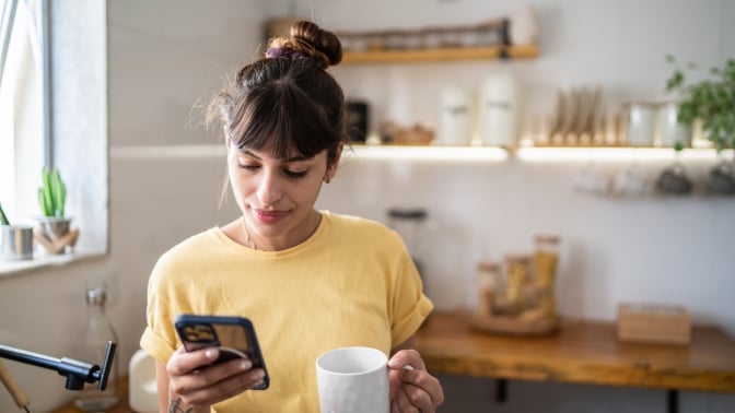 A woman looks at her phone in the kitchen.