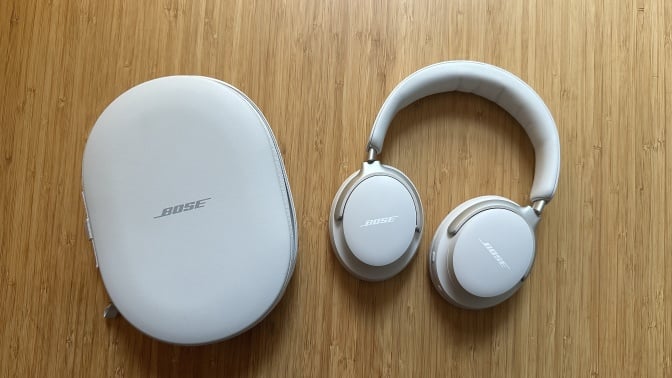 A pair of Bose QuietComfort Ultra headphones with case on wood surface