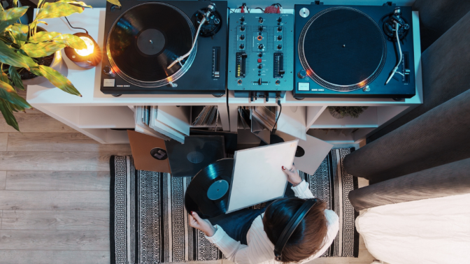 Top view of a person with headphones handling vinyl records beside a turntable.