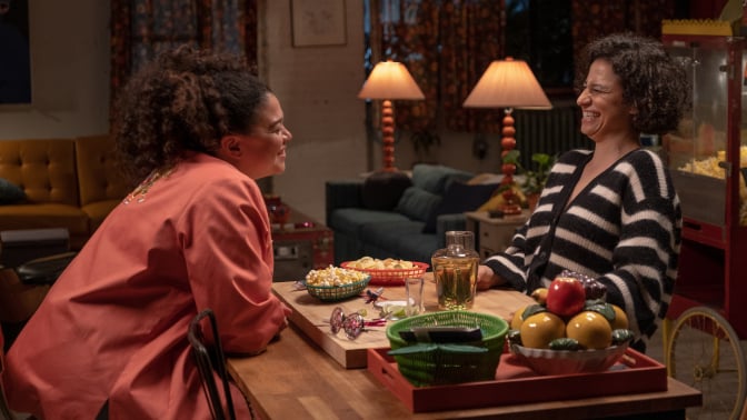 Still from 'Babes' shows Ilana Glazer and Michelle Buteau's characters laughing and sharing snacks.