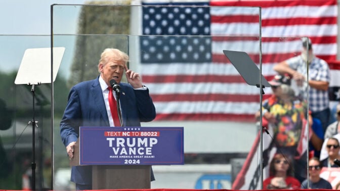 Donald Trump behind bulletproof glass at a campaign rally in 2024