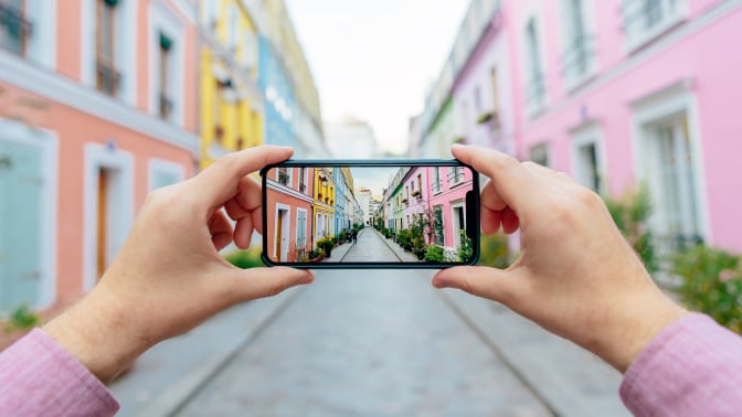 Personal perspective of a man photographing colorful street Rue Cremieux with smartphone.