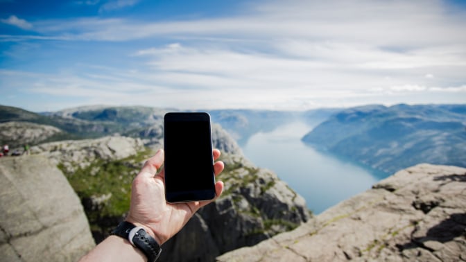 A person holds a phone up toward the horizon in a remote area.