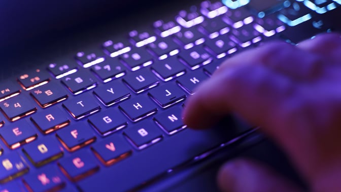 A person working on a neon computer keyboard with colorful backlighting.