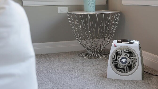 a vornado space heater sits on a carpeted floor in a brightly lit bedroom with natural light