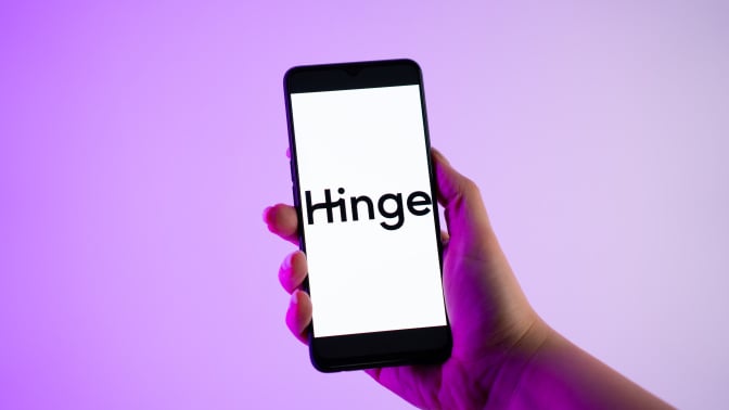 A person is holding a mobile phone with the Hinge logo on its screen