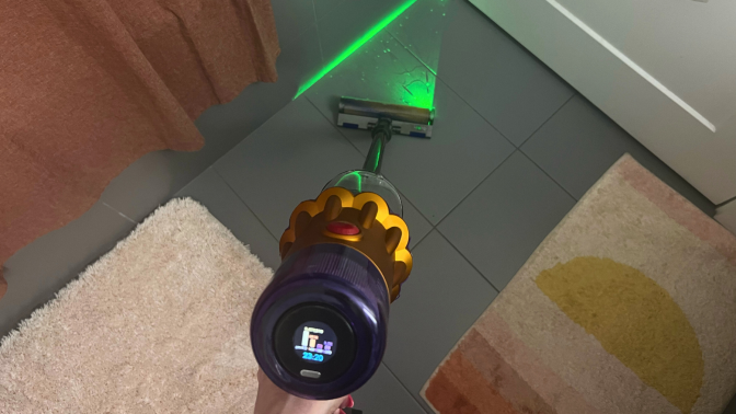 Hand cleaning tile bathroom floor with Dyson V12 Detect Slim vacuum and green laser highlighting debris on floor