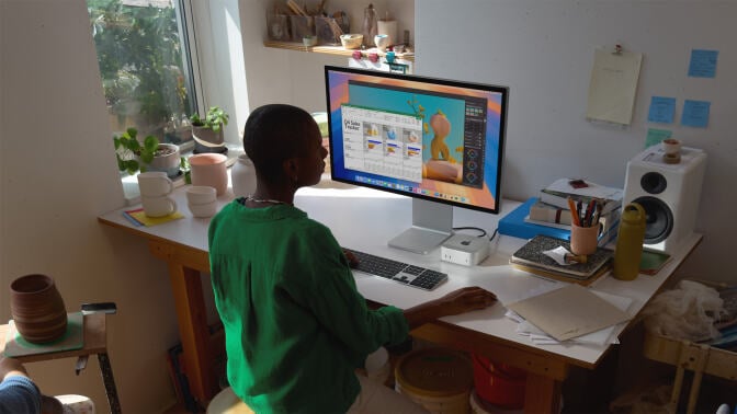 Person sitting at computer desk using Mac Mini and iMac