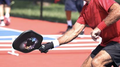 older man swinging pickleball racket on court