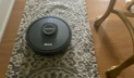 Gray Shark robot vacuum cleaning rug beside gold table legs