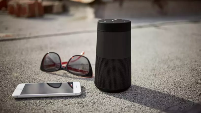 a Bose Soundlink Revolve II speaker, sunglasses, and a smartphone on a sidewalk